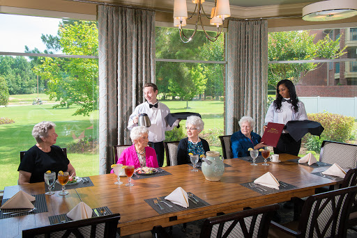A cheerful gathering of seniors enjoying a meal in an elegant dining room, attended by waitstaff.