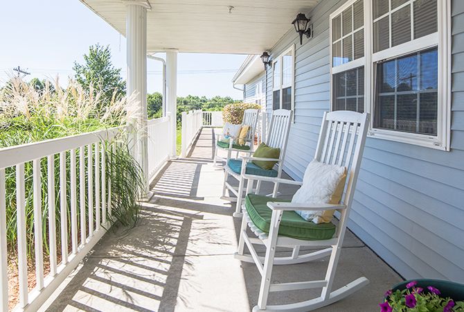 A sunny porch with white rocking chairs and pillows, perfect for relaxation.