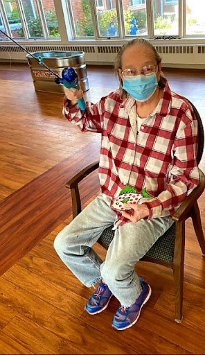 A person wearing a mask and a checkered shirt is sitting in a chair, holding a colorful object.