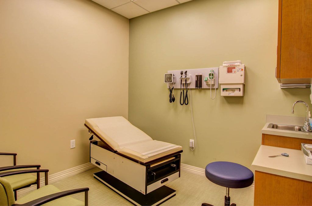 A medical examination room with an exam table and wall-mounted medical equipment.