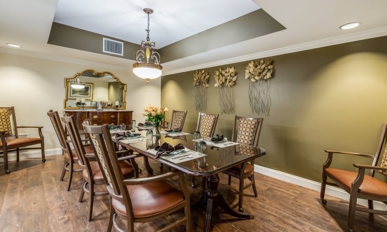 A well-decorated dining room with a large wooden table and elegant chairs, featuring warm lighting and sophisticated wall decor.