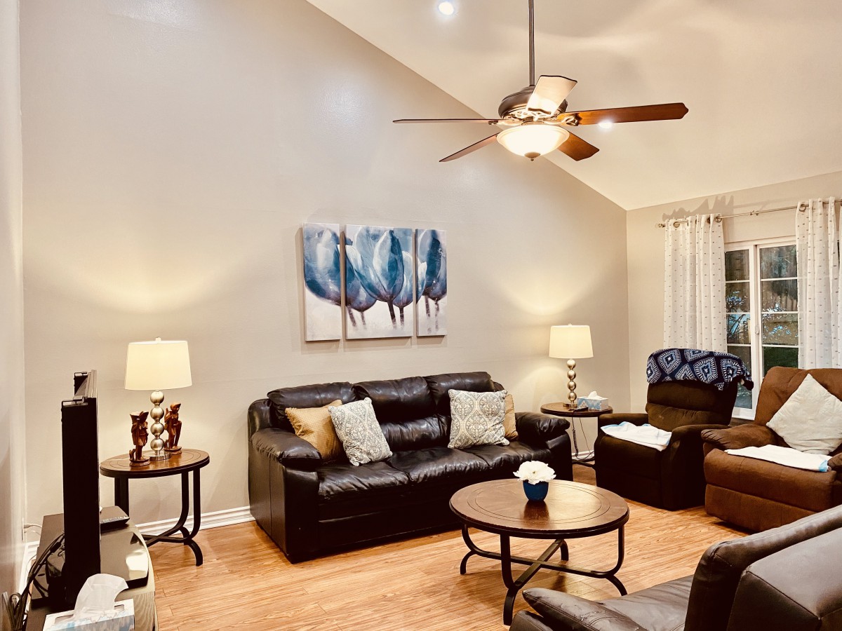 A cozy living room with a black leather sofa, matching armchair, wooden coffee table, decorative artwork, and soft lighting from lamps.