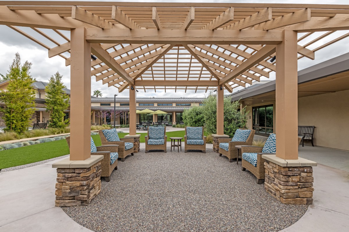A stylish outdoor patio featuring a pergola and comfortable seating surrounded by lush landscaping.
