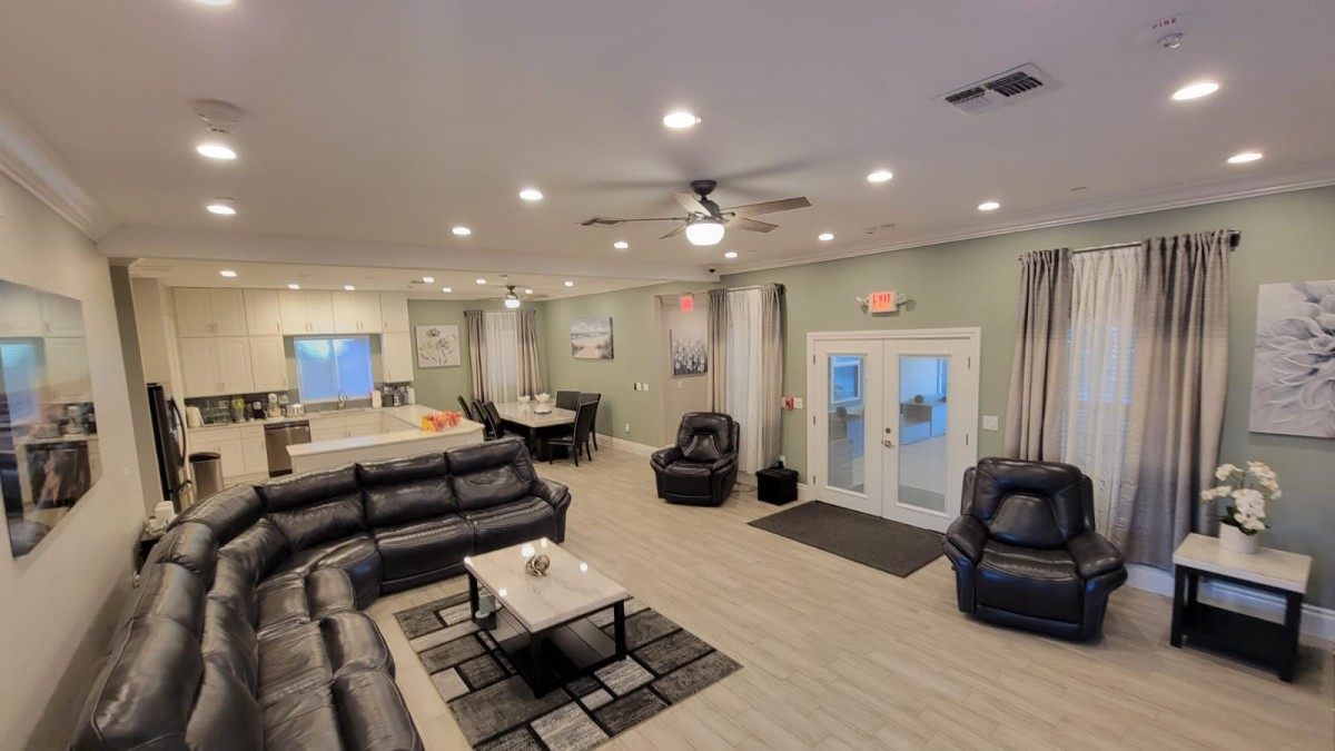A modern open-plan living room featuring leather sofas, a ceiling fan, and recessed lighting with an adjoining dining area.