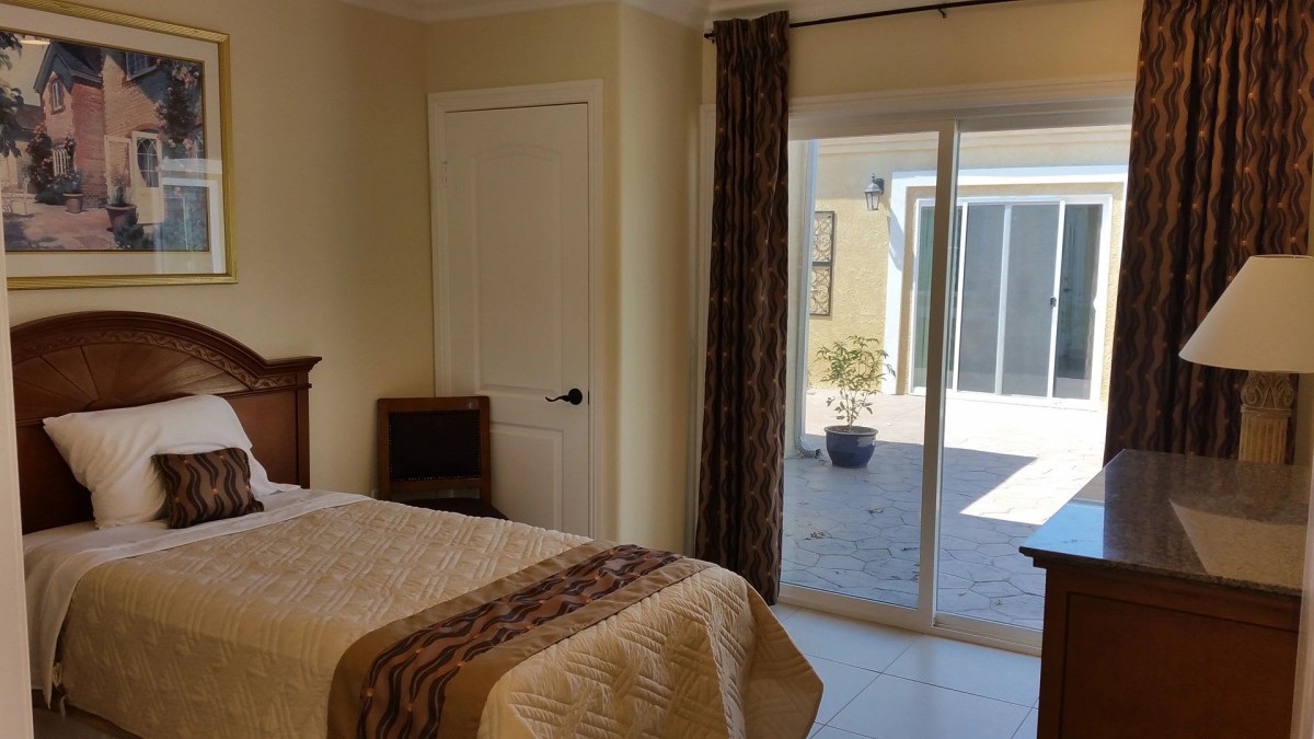A cozy bedroom with a bed, sliding glass door, and sunlight streaming in.