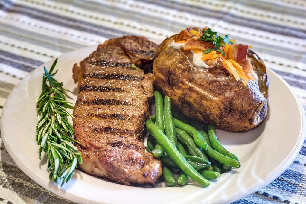A delicious dinner featuring a grilled steak, a baked potato with toppings, and a side of green beans.