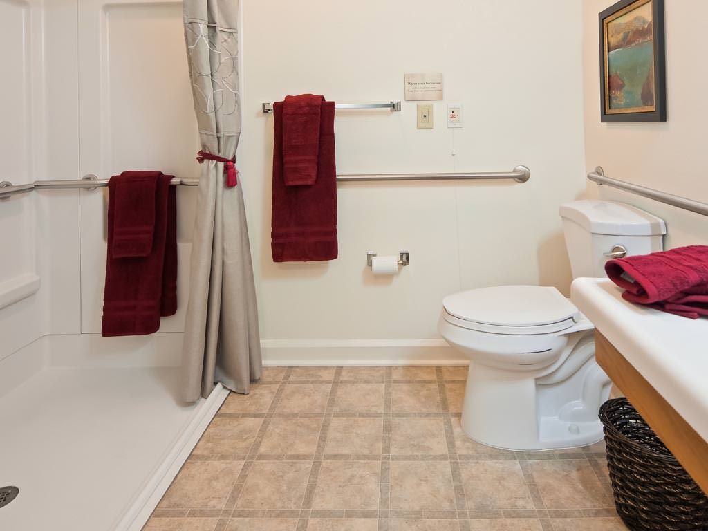 A clean bathroom with a tiled floor, featuring a toilet, shower area, and maroon towels.