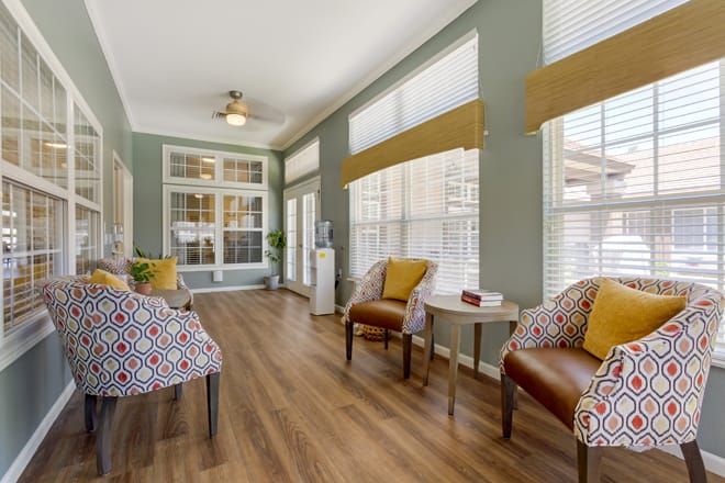 A cozy living room with ample natural light, featuring stylish chairs and a hardwood floor.