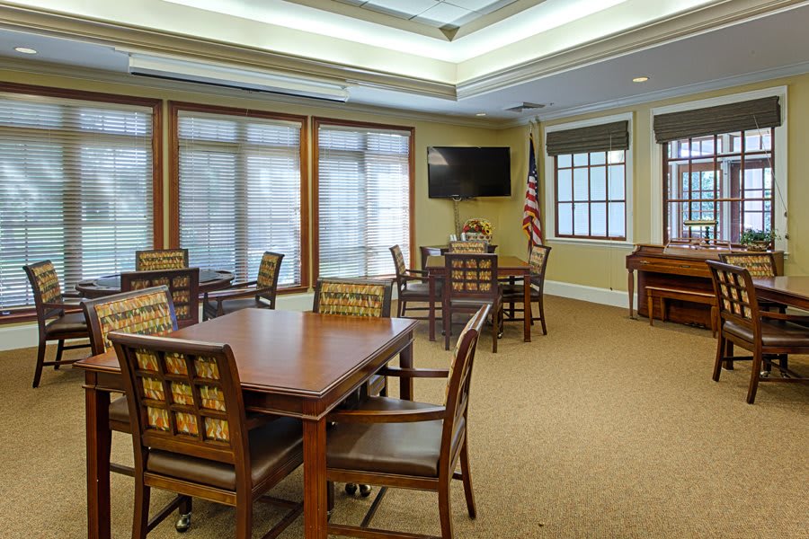 A well-lit conference room with multiple tables and chairs, featuring a television and large windows.