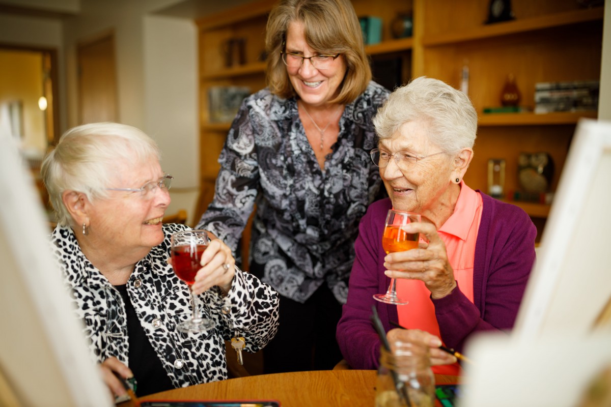 Three elderly women enjoying drinks and socializing together indoors.