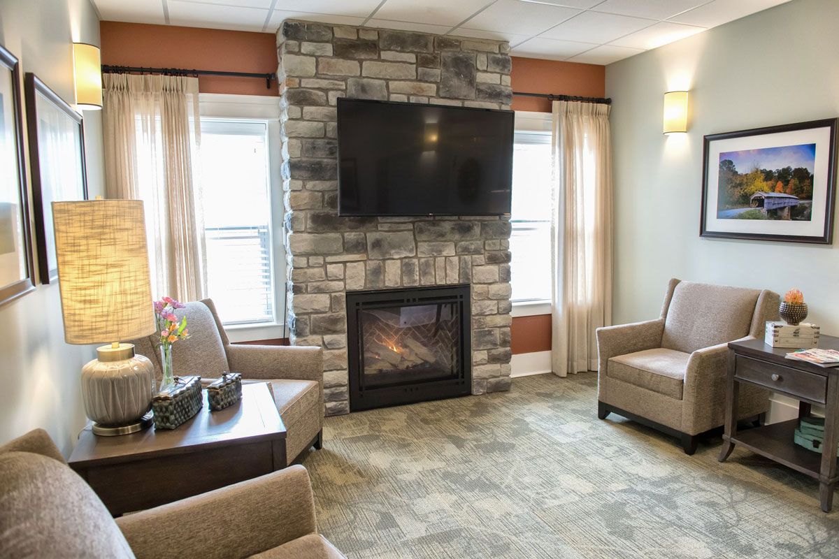 A cozy living room featuring a stone fireplace with a mounted television, surrounded by comfortable armchairs and large windows.