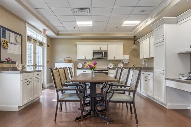 A modern kitchen and dining area featuring a wooden table with chairs, surrounded by white cabinets and a wood-paneled floor.