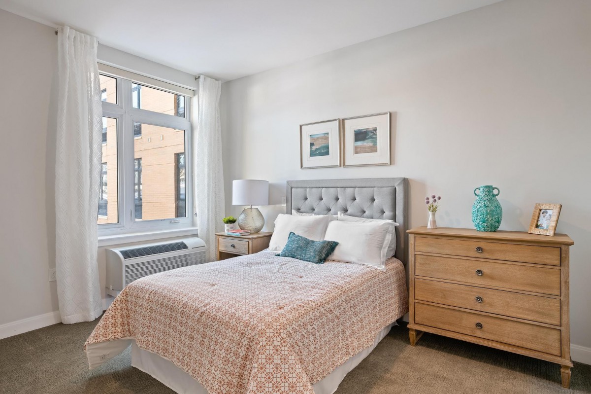 A bright, cozy bedroom with a plush bed, stylish decor, and natural light streaming through a large window.