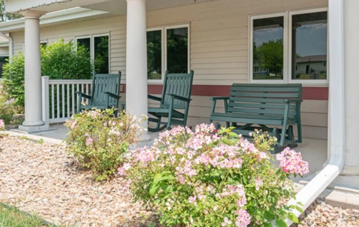 A charming porch with green rocking chairs and blooming flowers.