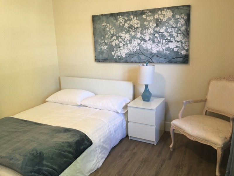 A minimalist bedroom featuring a bed, nightstand, lamp, and artwork on the wall.