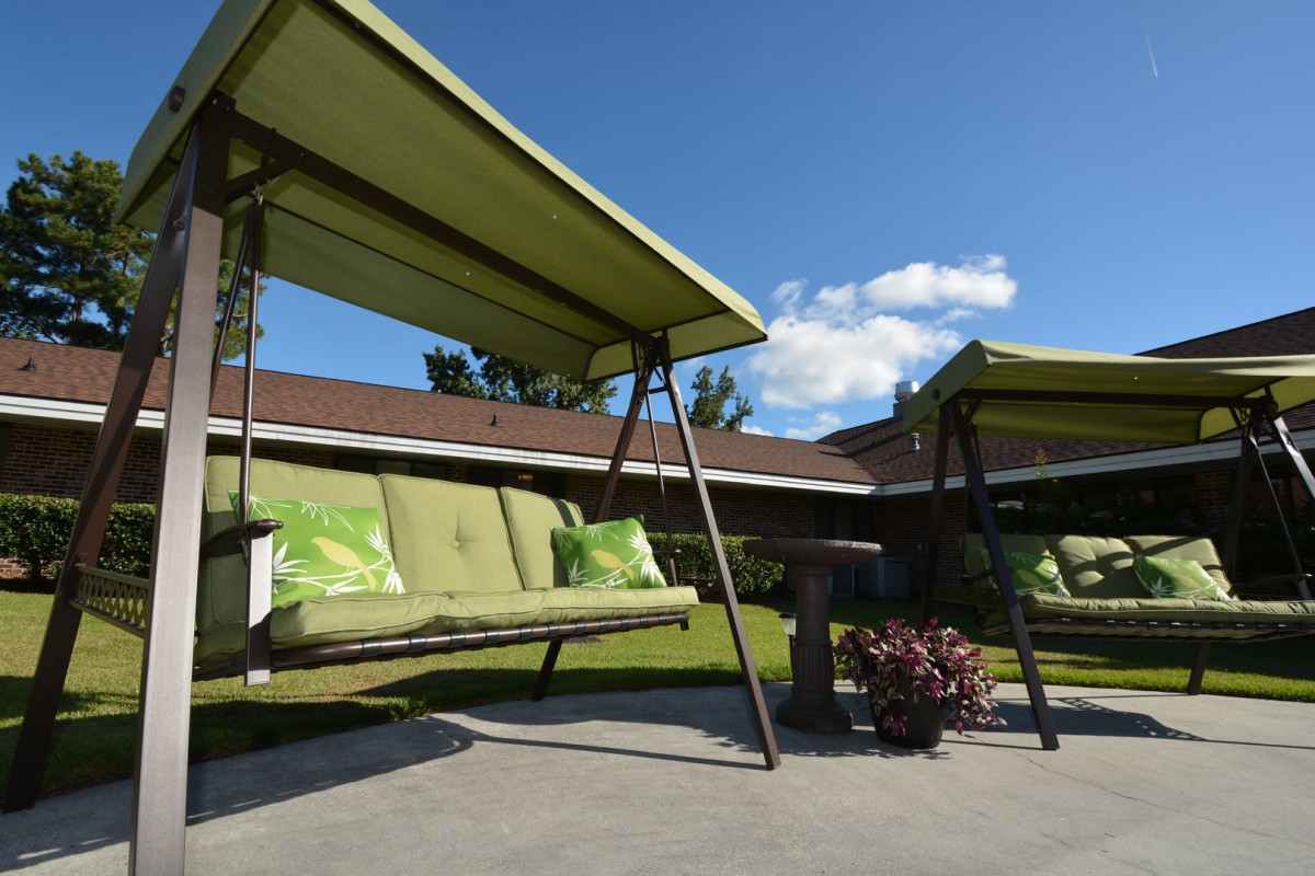 Two outdoor swings with green canopies and cushions on a sunny patio.