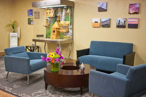 A cozy waiting room featuring comfortable blue sofas, a wooden coffee table adorned with flowers, and a decorative birdcage in the background.