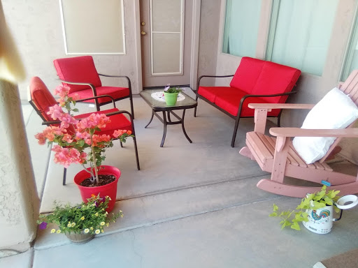 A cozy outdoor porch setup with red chairs, a small table, and colorful flowers.
