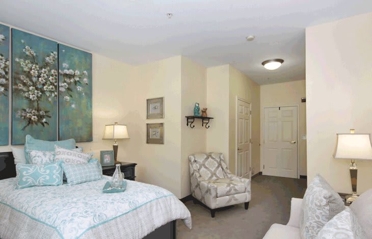A cozy bedroom with a bed, armchair, and decorative artwork on the walls.