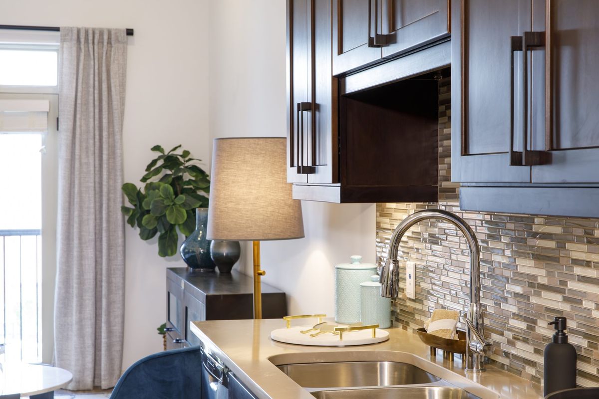 A modern kitchen interior featuring a countertop lamp beside the sink and dark wood cabinets.