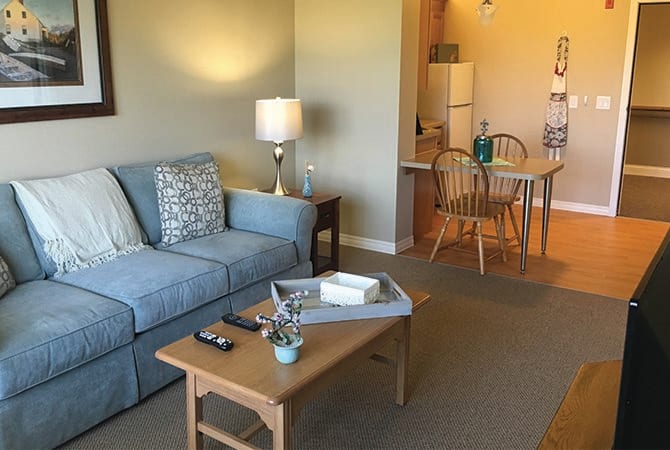 A cozy living room with a blue sofa, wooden coffee table, and a lamp, leading into an open dining area.