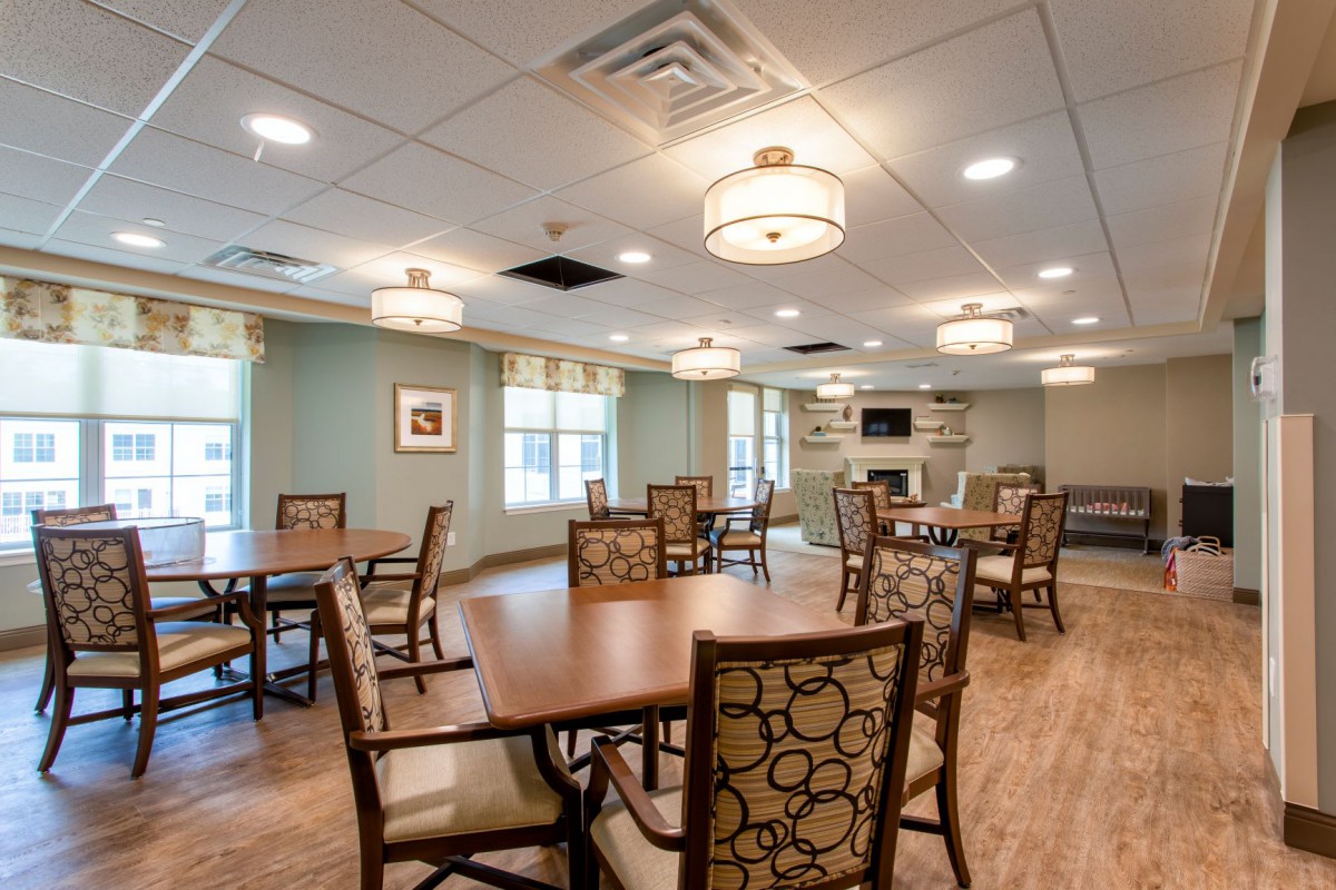 A spacious and well-lit dining room with multiple tables and chairs, featuring elegant ceiling lights and large windows.