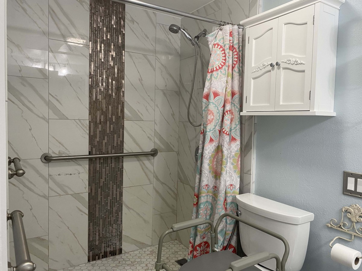 An accessible bathroom with a shower, grab bar, and floral curtain.