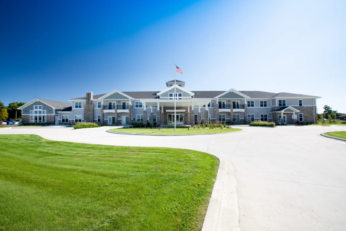 A grand mansion with a sprawling lawn and circular driveway under a clear blue sky.