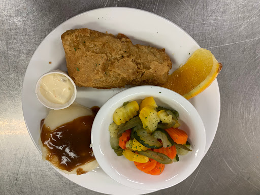 A well-balanced dinner plate featuring fried chicken, mixed vegetables, and a side of sauce with a slice of orange.