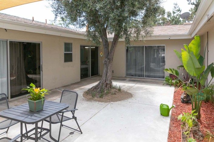 A cozy patio area with outdoor furniture and a tree, surrounded by the exterior of a house.
