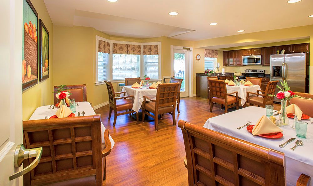 A cozy dining area with neatly arranged tables and chairs, wood flooring, and large windows with curtains.
