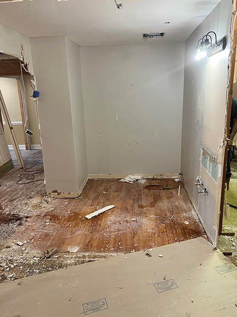 A room under renovation with exposed drywall and flooring debris.