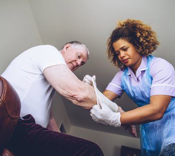 A nurse provides medical assistance to an elderly man at home.