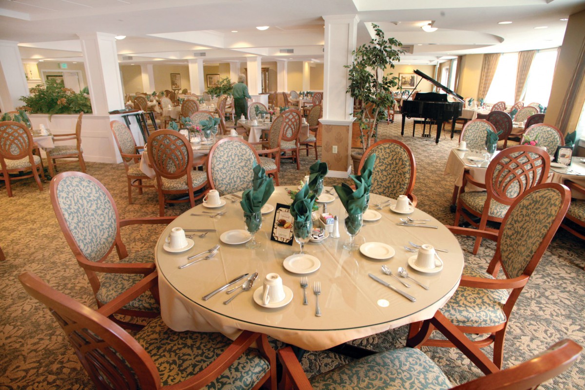 An elegantly set dining table in a spacious restaurant with a piano in the background.