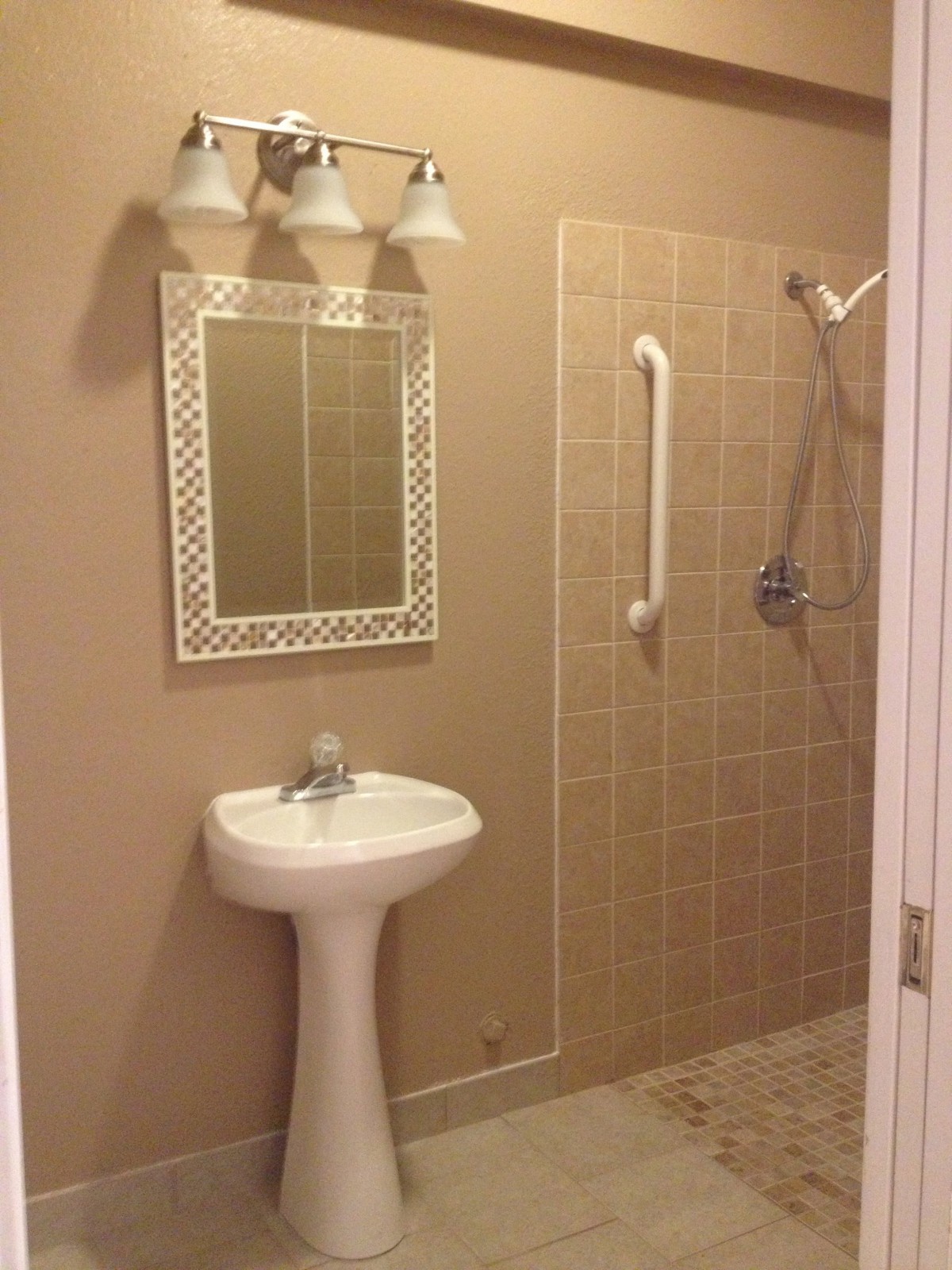 A bathroom featuring a sink, decorative mirror, and tiled shower area with a grab bar.