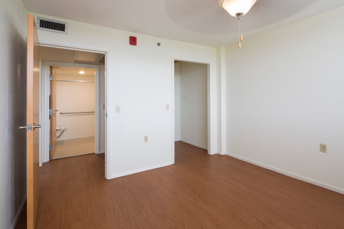 An empty room with wood flooring and white walls, featuring a doorway and ceiling light.