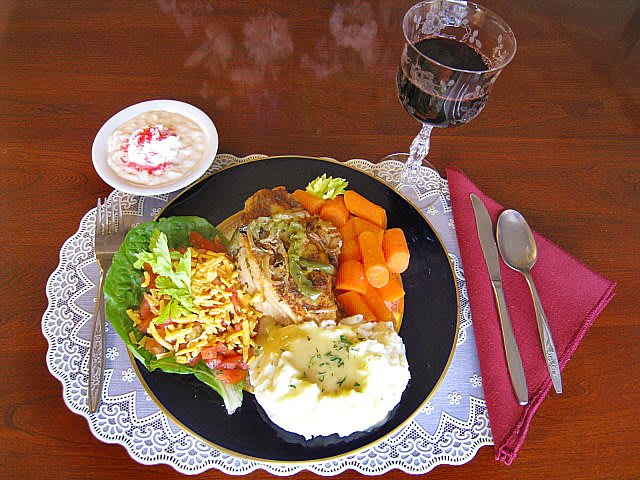 A well-presented dinner plate featuring a main course with salad, carrots, mashed potatoes, and a glass of red wine, accompanied by a dessert.