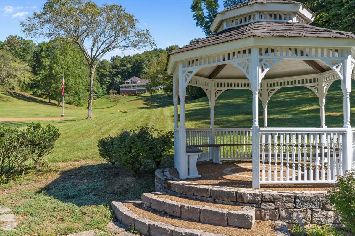 A serene park setting featuring a white gazebo surrounded by lush greenery and open fields.