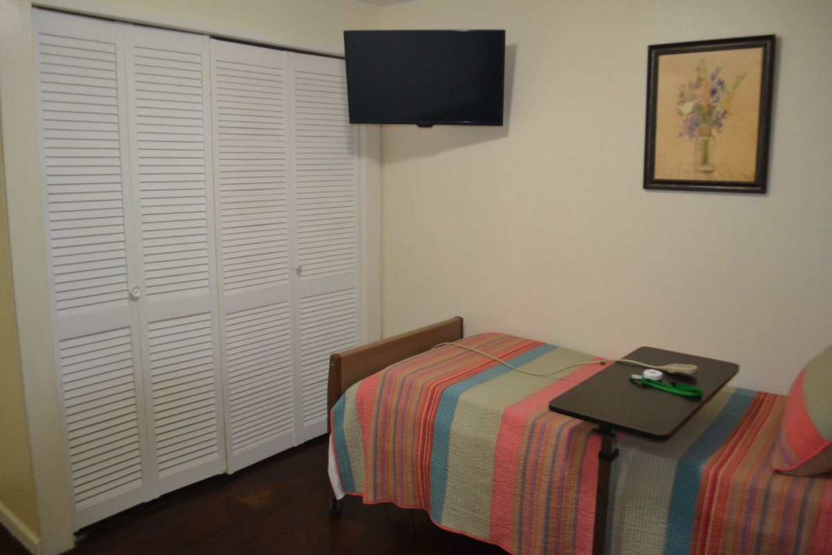 A small bedroom with a single bed, a wall-mounted TV, and a colorful striped bedspread.