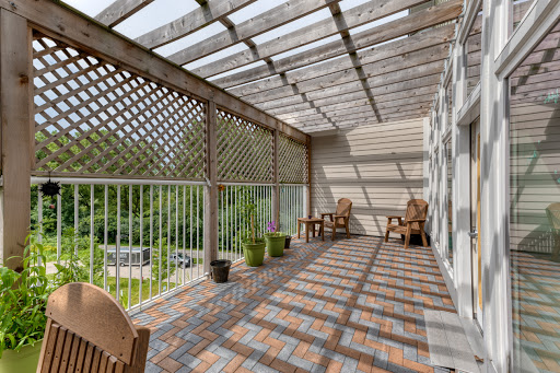 A serene balcony furnished with wooden chairs and surrounded by greenery, adorned with a lattice overhead that casts playful shadows.