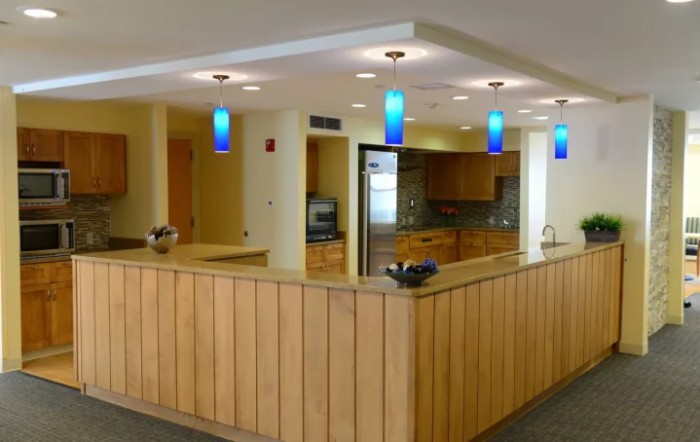 A modern reception area with wood paneling, blue pendant lights, and an adjacent kitchen space.