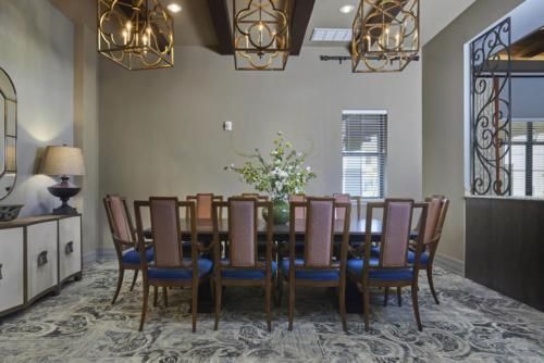 A stylish dining room featuring a large table surrounded by chairs, elegant chandeliers, and a vase of flowers in the center.