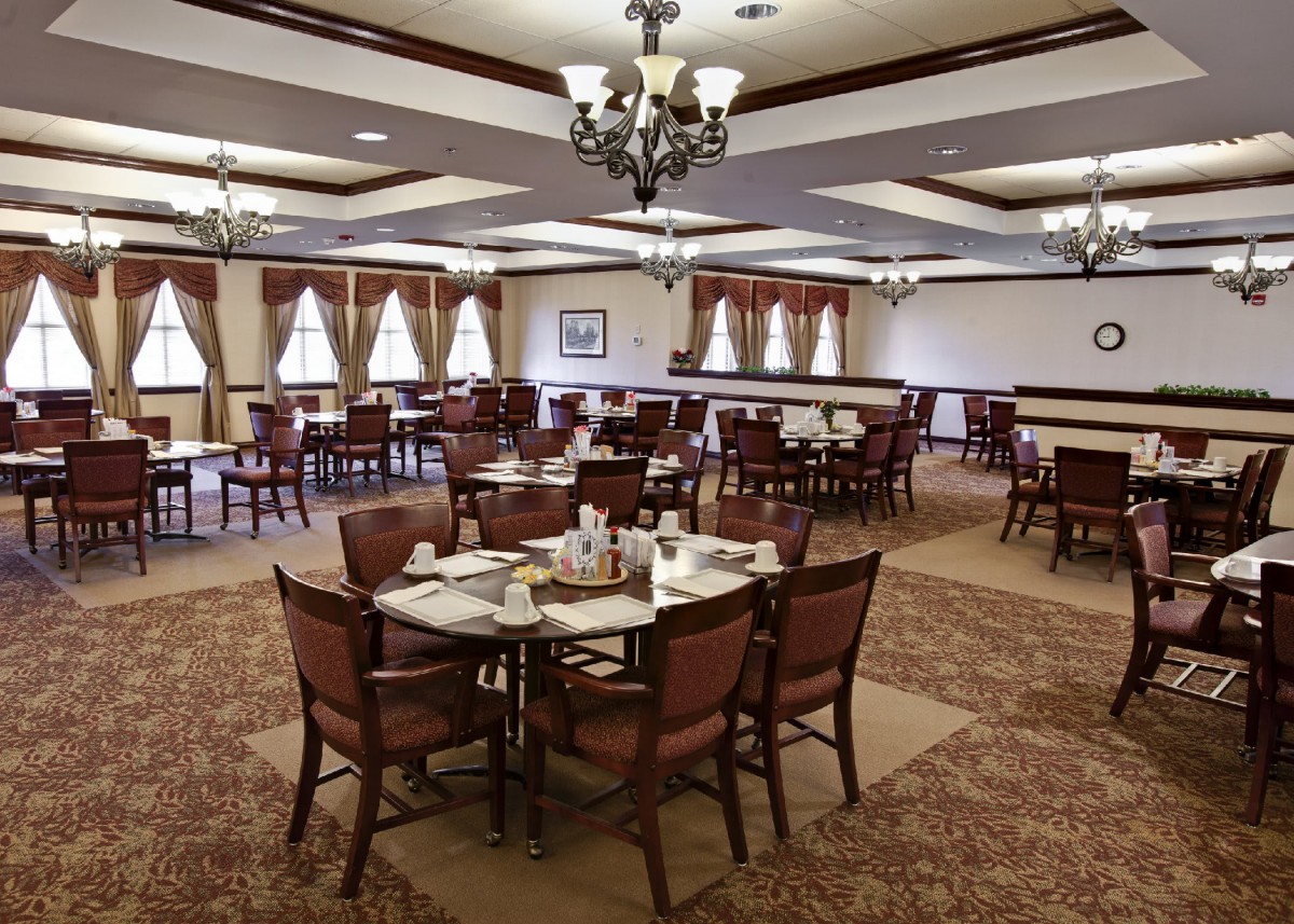 Elegant dining room with neatly arranged tables and chairs, featuring chandeliers and large windows.