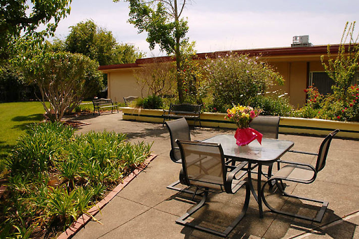A serene outdoor space featuring a table and chairs surrounded by lush greenery and vibrant flowers.