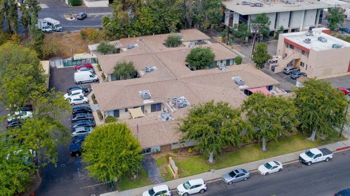 Aerial view of a residential complex with adjacent parking and surrounding trees.