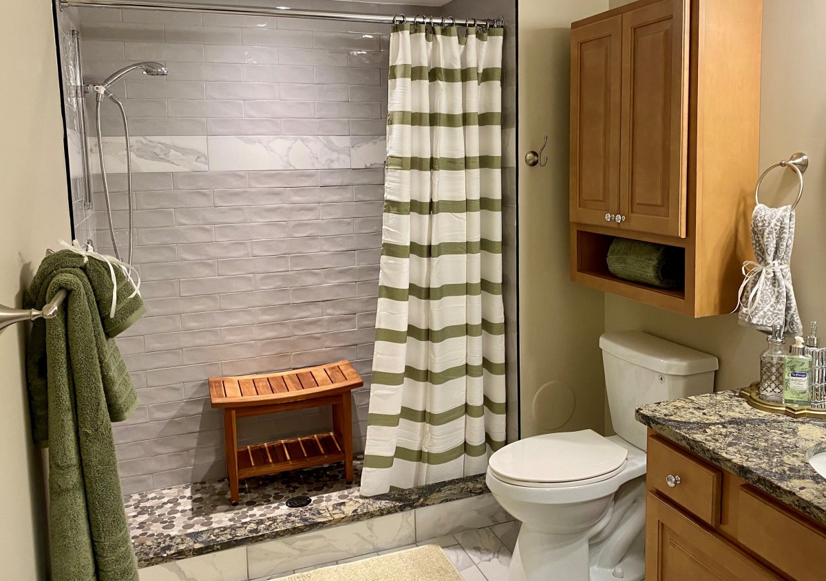 A modern bathroom with a shower, toilet, and wooden bench.