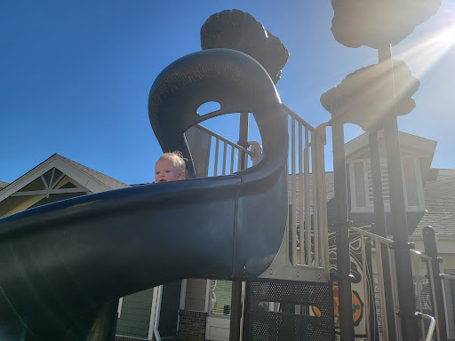 A child peeks out from the top of a playground slide under the clear blue sky.