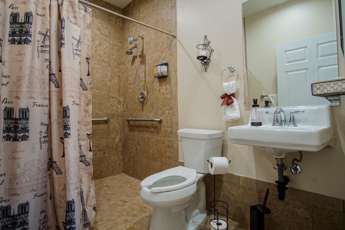 A neatly organized bathroom with a toilet, shower, sink, and handrails.