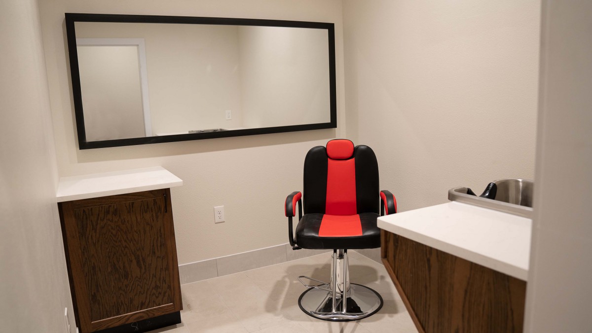 An empty barbershop or hair salon with a stylish red and black barber chair in front of a large mirror.