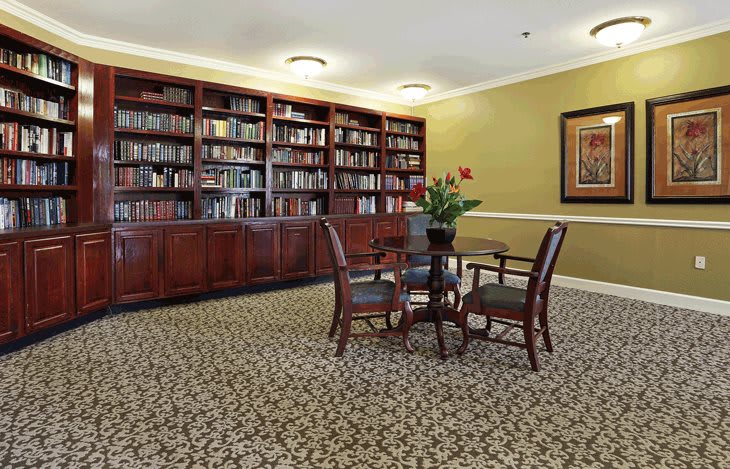 A cozy library corner with a large bookshelf and a small table surrounded by chairs.
